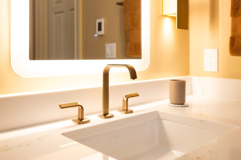 An upscale bathroom remodel with white countertop and gold hardware.